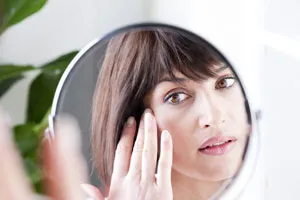 A woman looking at herself in a mirror and touching her face